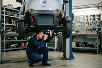 Technicien automobile inspectant le dessous d'une voiture sans permis électrique surélevée sur un pont de garage professionnel