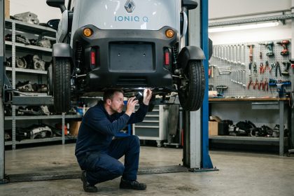 Technicien automobile inspectant le dessous d'une voiture sans permis électrique surélevée sur un pont de garage professionnel